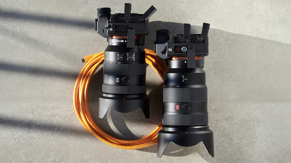 Two telephoto lenses displayed with an orange camera strap arranged in a circular composition on concrete.