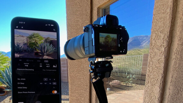 Smartphone displaying exposure bracketing settings next to a mirrorless camera mounted on a tripod.