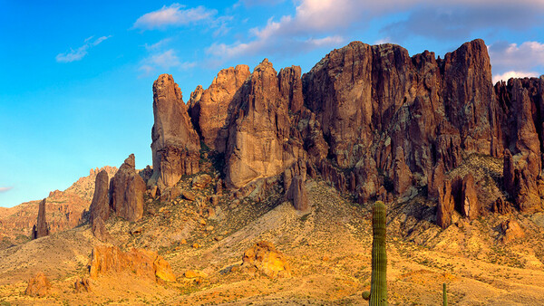 Towering desert rock formations with a saguaro cactus in the foreground under clear blue sky.