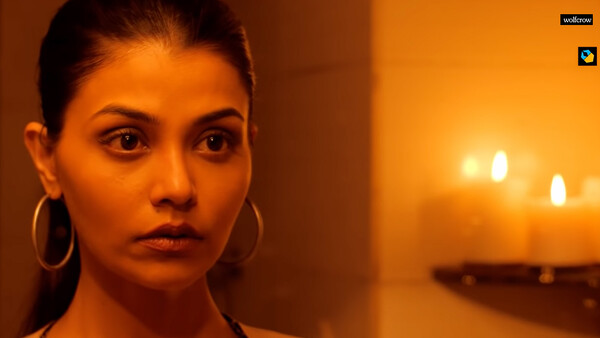 Woman with serious expression against warm orange-toned backdrop with bokeh lights.