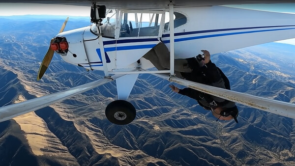 Skydivers exiting a small aircraft above mountainous terrain during daylight.
