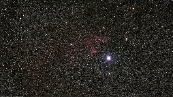 Deep space photograph showing a bright star surrounded by nebulosity and countless smaller stars against a dark starfield.