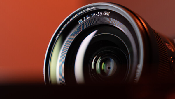 Close-up of a Sony E-mount lens with f/2.8/16-35 GM specifications against a warm orange background.
