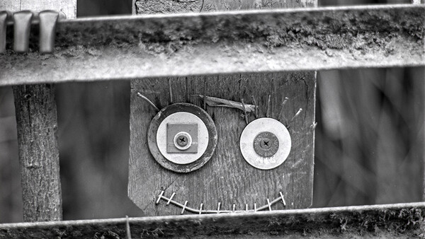Found-object art face made from circular metal discs and stitched line on wooden boards.