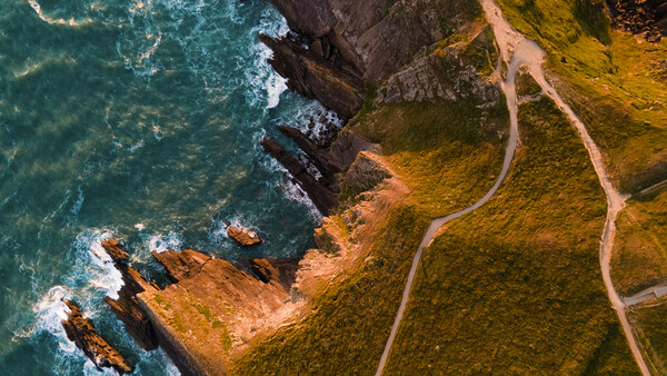 Aerial view of a winding coastal road along steep cliffs meeting turquoise ocean waves.
