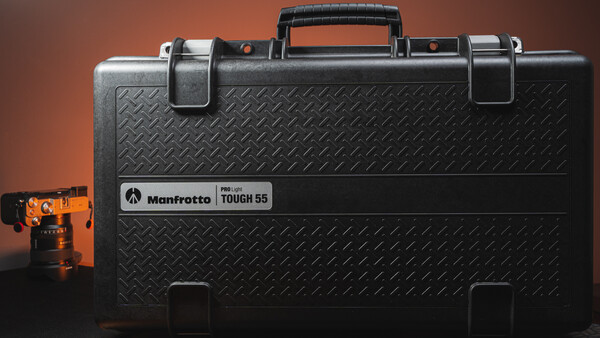 Manfrotto Tough 55 hard case with orange camera head shown on warm brown background.