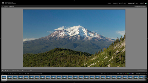 Snow-capped volcanic mountain rising above forested foothills under clear blue sky.