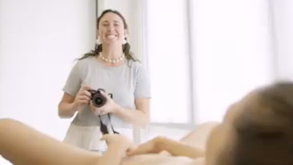 Photographer holding a camera while instructing a student in a bright studio setting.