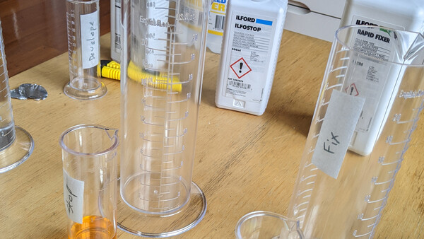 Laboratory cylinders and bottles with chemical solutions arranged on a wooden workbench.