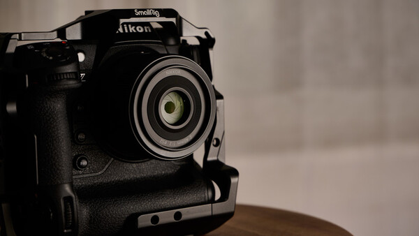 Black Nikon DSLR camera with Smallrig cage mounted on wooden surface against blurred background.