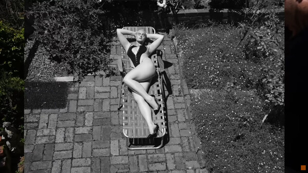 Overhead view of a woman lying in a wooden crate on a textured ground surface.