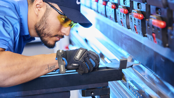 Technician in work gloves inspecting equipment panel with illuminated controls and indicators.
