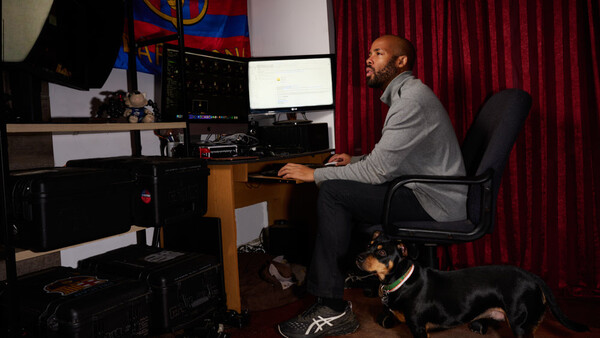 Man working at a computer desk in a content creation studio with professional lighting and red curtains.