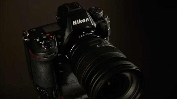 Black Nikon DSLR camera with telephoto lens mounted, photographed against dark background.