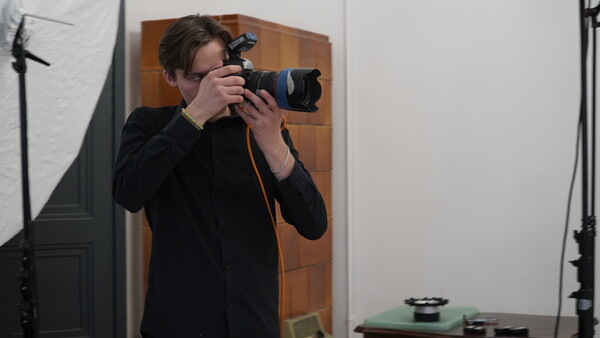 Photographer holding a DSLR camera with telephoto lens in a studio setting with professional lighting equipment.