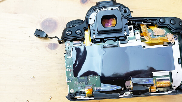 Disassembled camera showing internal circuitry, mirror mechanism, and sensor components on wooden surface.