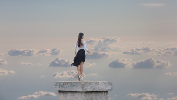Woman standing on concrete pillar against dramatic cloudy sky.