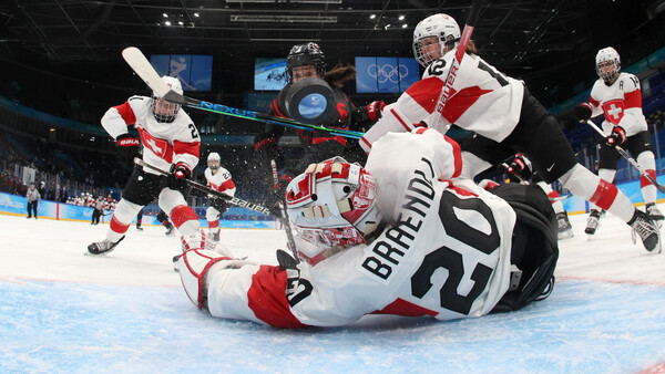 Hockey goalie in red and white uniform sprawled on ice after a save attempt during competitive match.
