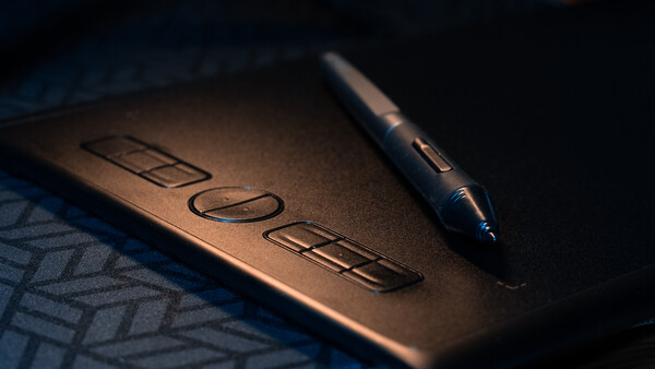 A dark pen rests on a notepad with embossed text under dramatic side lighting.