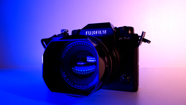 Fujifilm mirrorless camera with illuminated lens against blue and pink gradient background.