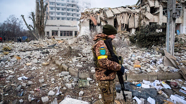 Soldier in camouflage walking through rubble of destroyed residential buildings.
