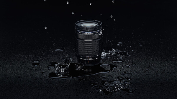 Telephoto lens surrounded by water droplets and debris on dark wet surface.