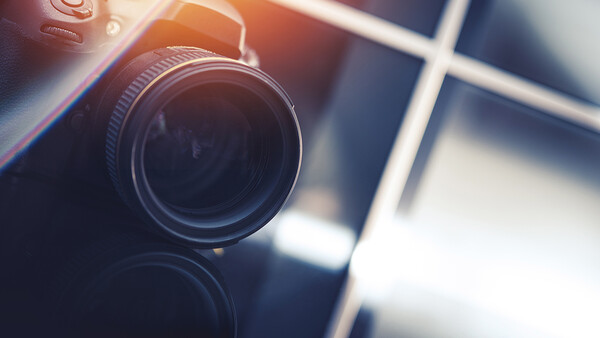 Close-up of a camera lens with warm golden sunlight and window shadows in the background.