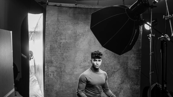 Man in casual shirt positioned in studio with large softbox and reflector lighting setup.
