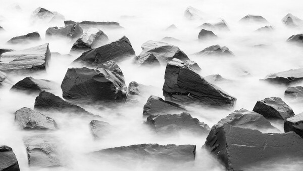 Rocks partially submerged in flowing water with long exposure effect creating smooth, misty texture.