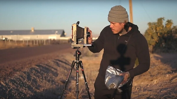 Photographer with vintage camera on tripod in open field during golden hour.