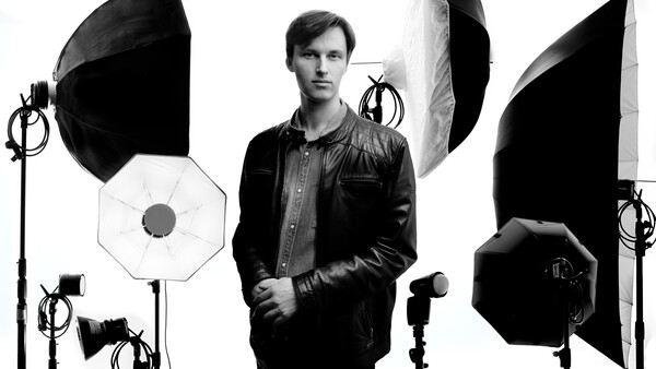 Man in leather jacket posed among professional studio lighting equipment and softboxes.