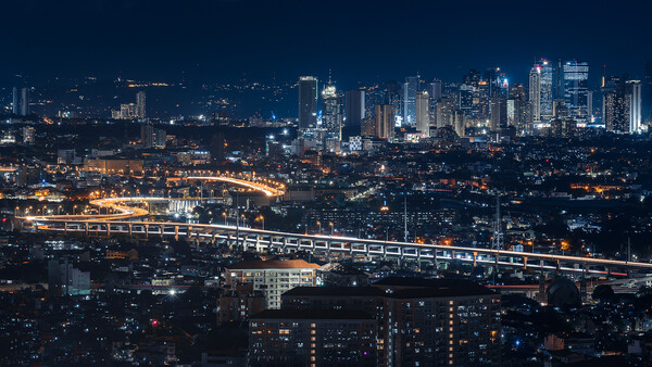 City skyline at night with illuminated bridge spanning across foreground and downtown towers glowing in background.
