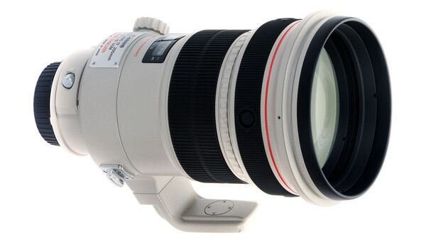 White telephoto lens with internal focus mechanism and red ring accent, shown in profile against white background.
