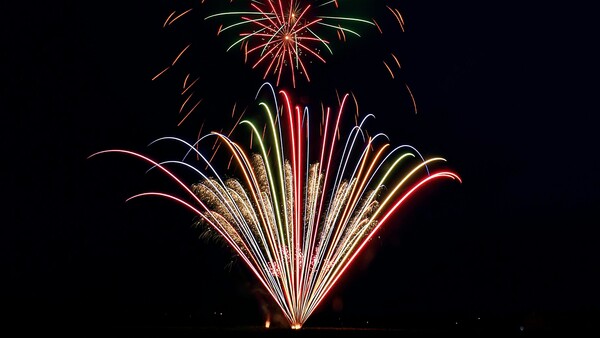 Vibrant fireworks burst across a dark night sky in red, gold, green, and white colors.