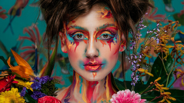 Portrait with vibrant face paint and colorful flowers surrounding the subject against a teal background.