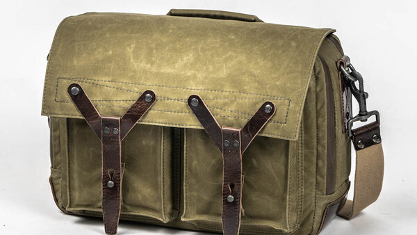 Waxed canvas messenger bag with brown leather straps and brass hardware on white background.