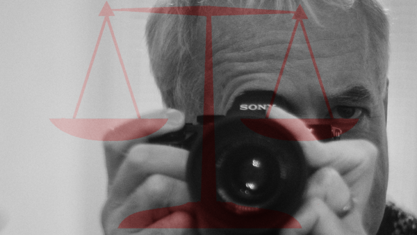 Photographer holding a Sony camera with scales of justice overlay in red and black.
