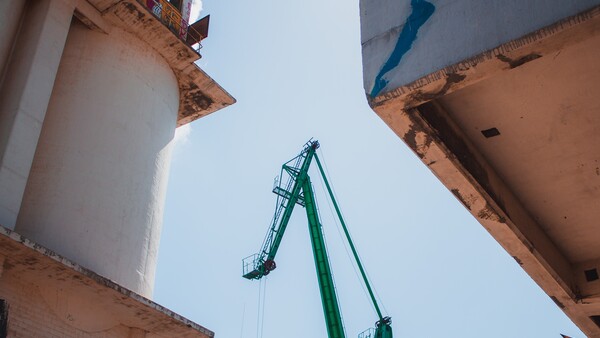 Green industrial crane extending upward against white cylindrical storage tanks and blue sky.