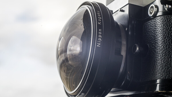Close-up of a vintage rangefinder camera lens showing focus ring and aperture markings against overcast sky.