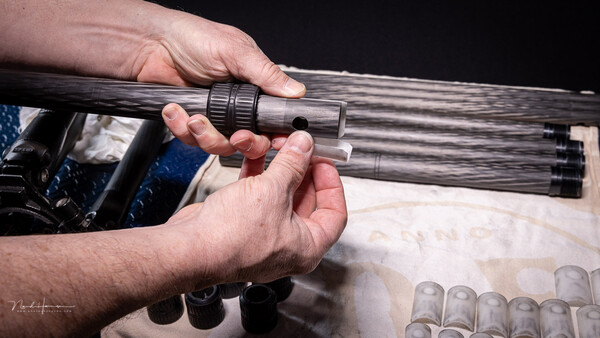 Two hands examining a wooden rifle barrel with threaded muzzle attachment during equipment inspection.