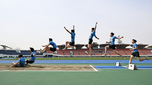 Young athletes in blue uniforms perform long jump attempts on an outdoor track and field stadium.