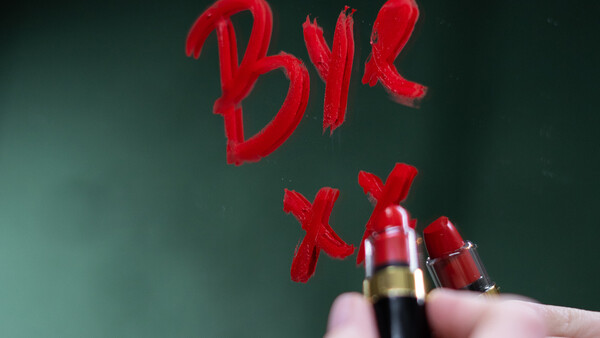 Red lipstick and cosmetic products with handwritten "BYE" text on green background.