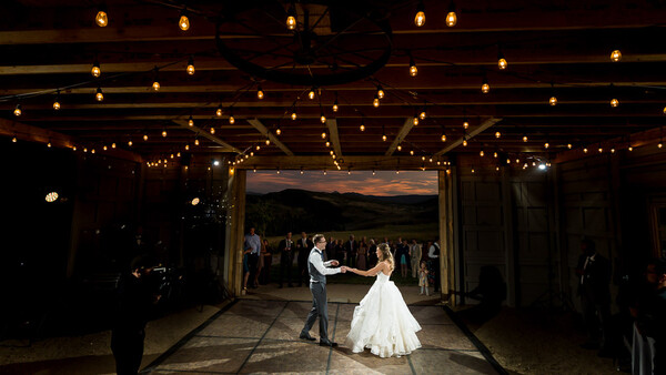 Bride and groom share their first dance under string lights in an open-air venue at dusk.
