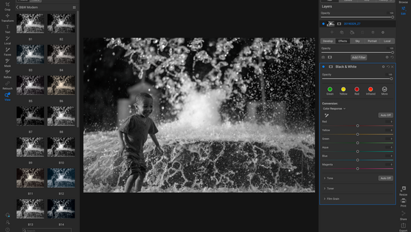 Child running through water spray in black and white photograph.