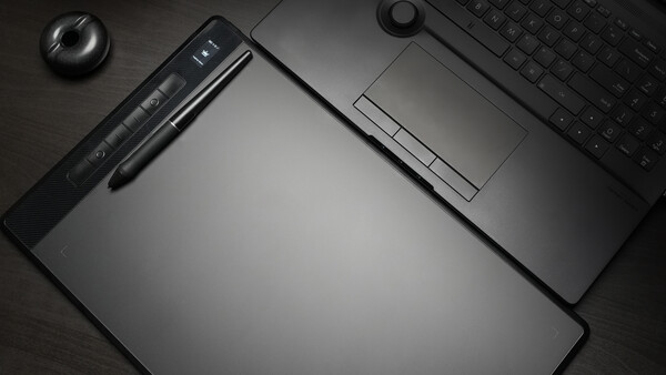 Overhead flat lay of creative workspace with graphics tablet, stylus, keyboard, and mouse on dark surface.