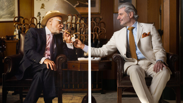 Two men in suits seated in leather chairs having a conversation in an elegant interior.