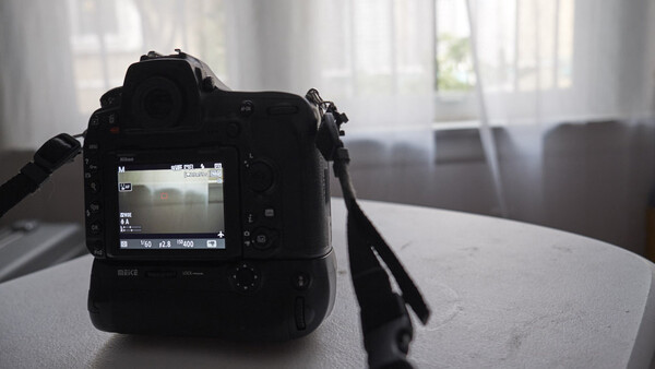 Professional DSLR camera with rear LCD screen visible, positioned on a table near a window with natural light streaming in.