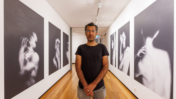 Photographer standing in gallery hallway with black and white portrait prints on both walls.
