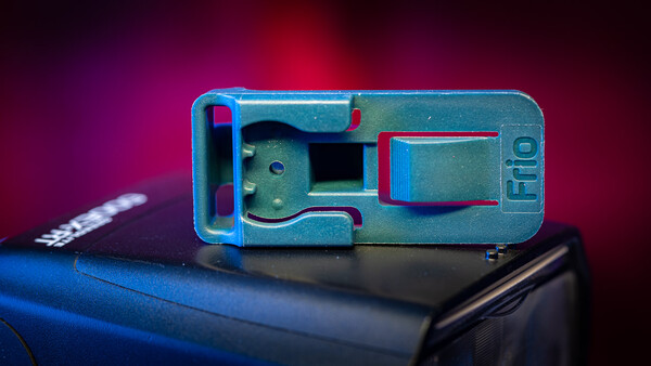 Disassembled blue and teal mechanical camera or device component against a dark background with magenta lighting.