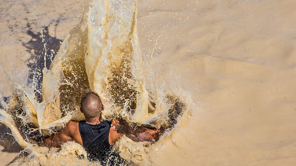 Person wading through turbid water with powerful wave splash creating dramatic white foam around them.